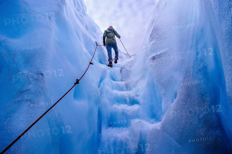 Woman walking steps out of a ice cave in Fox Glacier