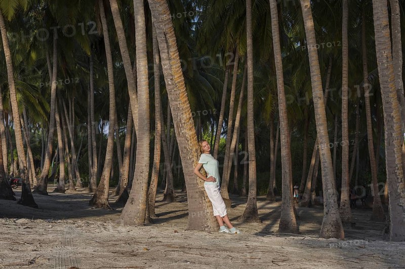 Young beautiful woman leaning on a palm tree in a tropical forest by the beach