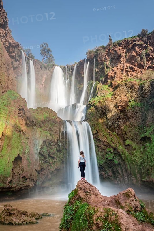 Young woman standing on a stone in front of Ouzoud waterfalls and cascades