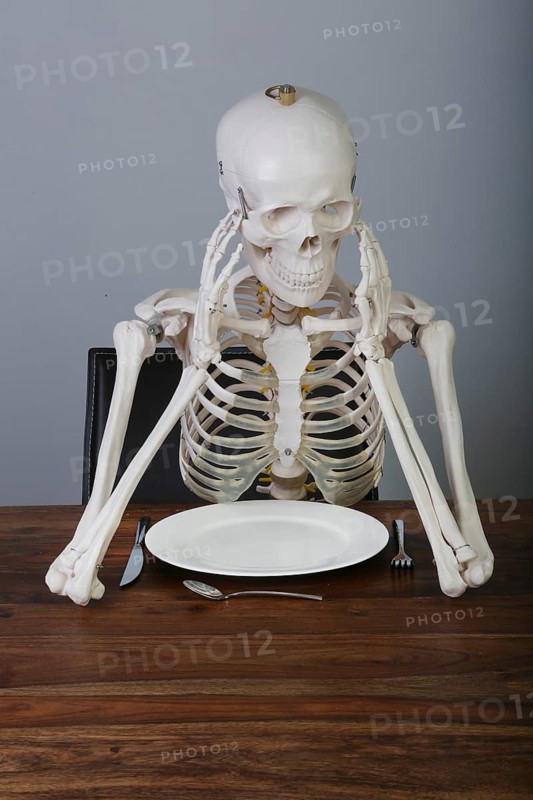 Skeleton with supported head sitting at table