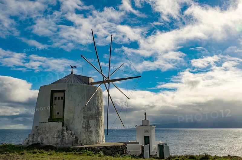 White windmill at the sea in front of a cloudy sky