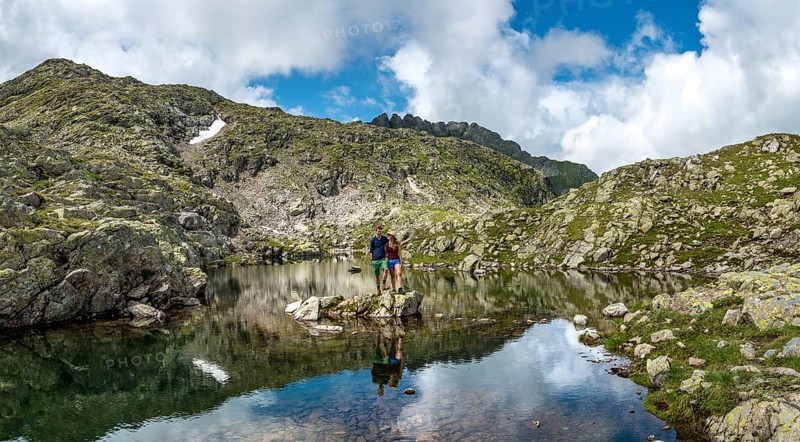 Couple hikers stands on a stone in a small lake