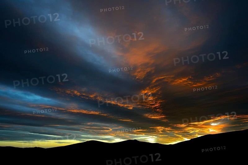 Dramatic sunset with rising storm clouds in front of mountain silhouette