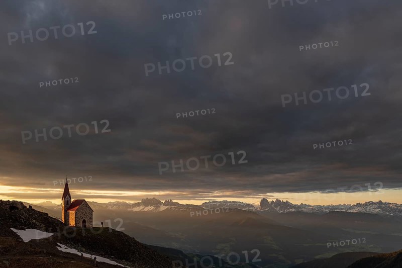 Latzfonser cross chapel at sunrise with dramatic clouds and South Tyrolean mountains