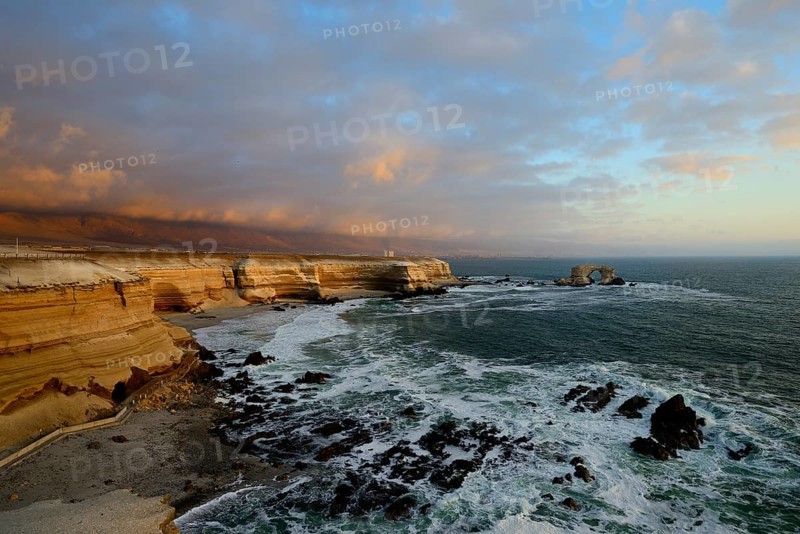 Rocky coast with arch La Portada at sunset with clouds