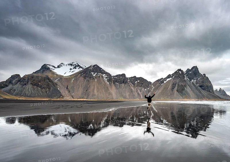 Hiker jumps at the black sandy beach