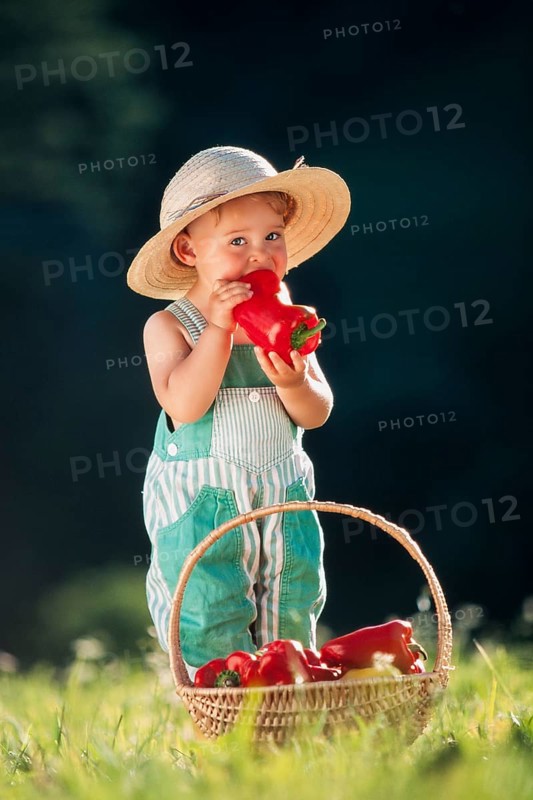 Three-year old girl with straw hat biting into a pepper