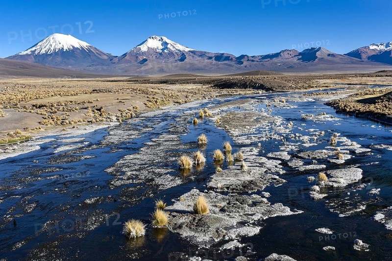 Snow-covered volcanoes Pomerape and Parinacota with icy river