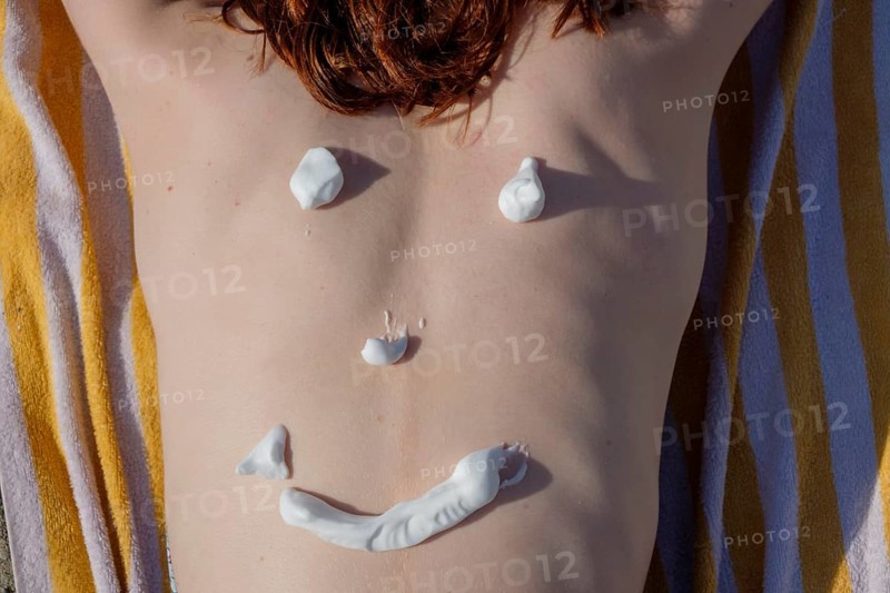 Red-haired young woman with sun cream on her back