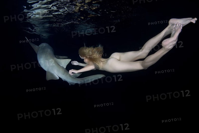 Nude beautiful woman swimming at night with a shark