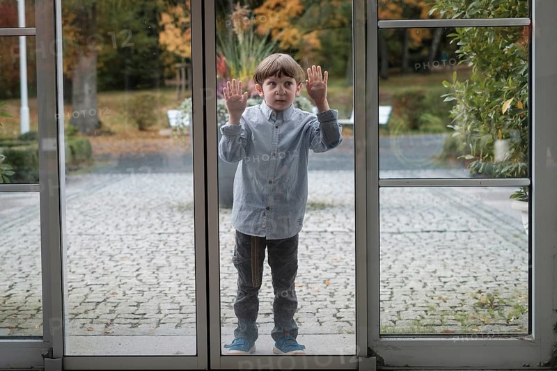 Child squeezes nose and hands on glass panel