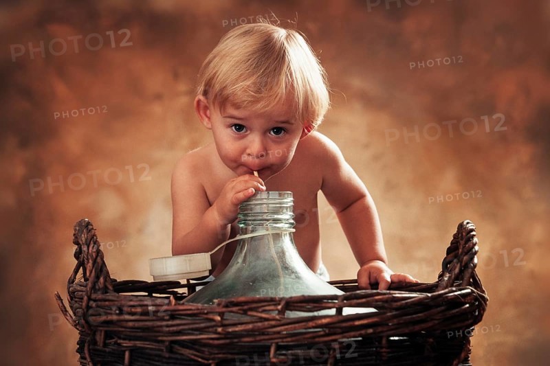 Three year-old girl drinking through a straw from glass carboy