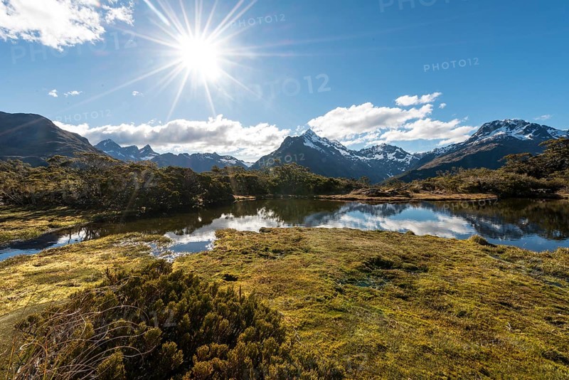 Sun shining on small mountain lake with reflection of a mountain chain