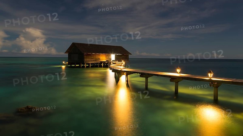 Wooden hut on stilts in lagoon at night