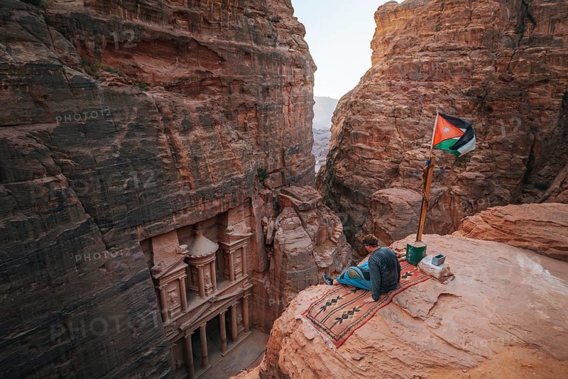 Tourist sits at the edge of a rock and looks from above into the canyon Siq