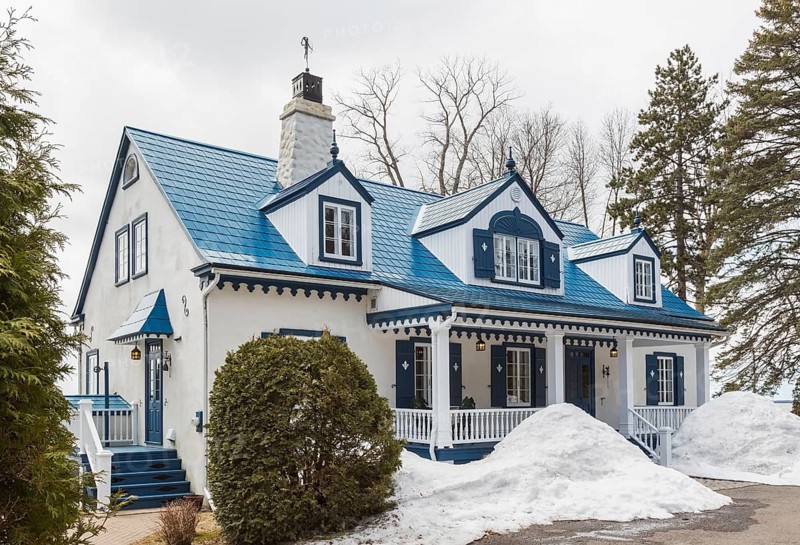 Old 1920s white roughcast with blue trim cottage style home facade with blue steel tile roof in early spring