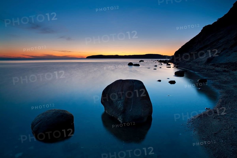 Coastline with big boulders on beach at sunset