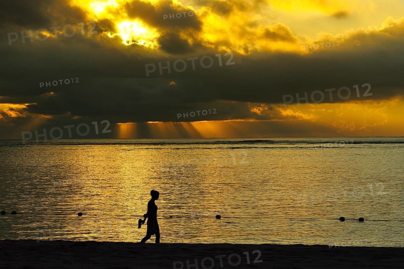 Woman walking at sunset with cloudy atmosphere on the beach Le Morne