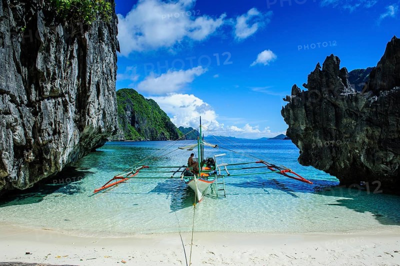 Outrigger boat on a little white beach and crystal clear water in the Bacuit archipelago
