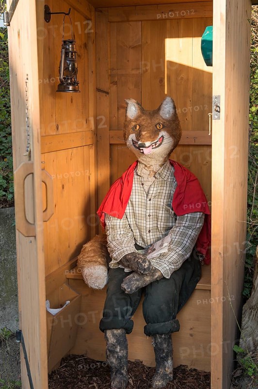 Straw doll fox sitting in outhouse