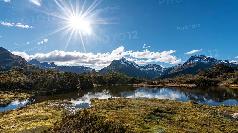 Sun shining on small mountain lake with reflection of a mountain chain
