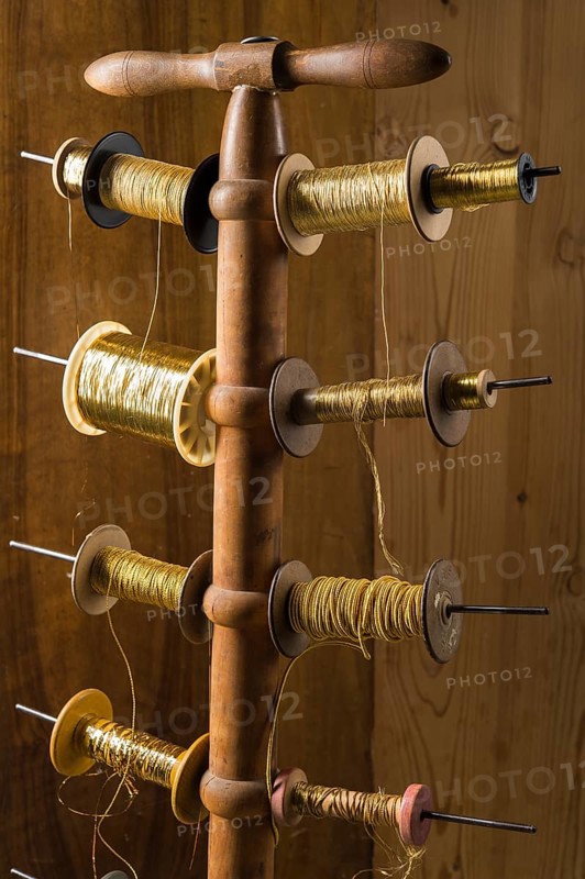 Thread stand in front of wooden wall with various gold and yellow yarns