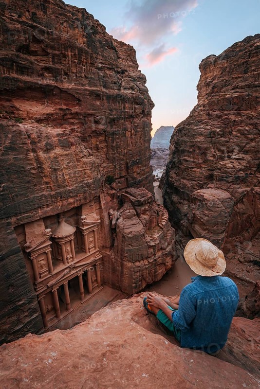 Tourist sits at the edge of a rock and looks from above into the canyon Siq