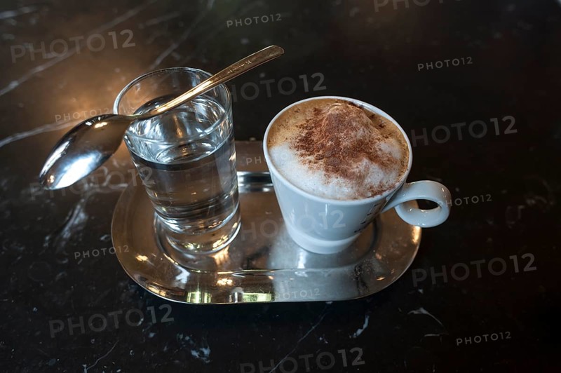 Cappuccino with cocoa powder and glass of water on marble table