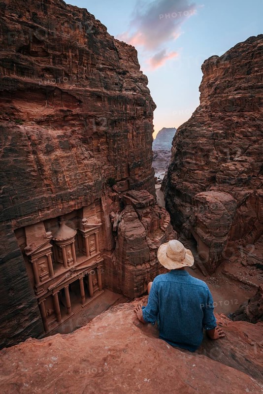 Tourist sits at the edge of a rock and looks from above into the canyon Siq