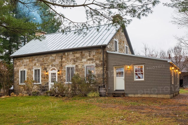 Old 1820 cottage style cut stone and fieldstone house facade with cedar shingles extension in autumn