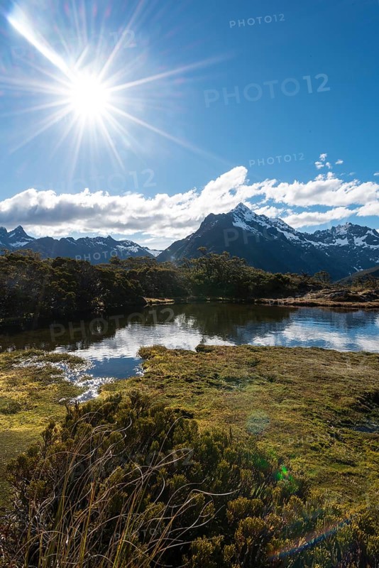 Sun shining on small mountain lake with reflection of a mountain chain
