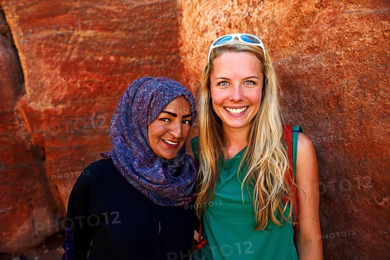 Tourist girl poses with local bedouin girl at colourful rock-formations in Petra