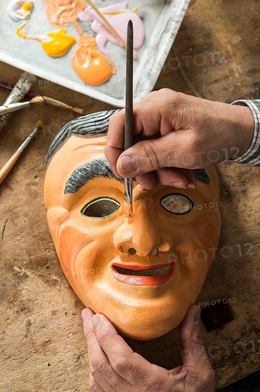 Painting the face of a wooden mask with a paintbrush