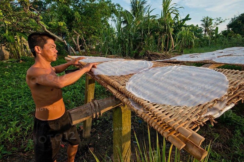 Vietnamese worker spreads steaming rice noodle patties on bamboo frame to dry