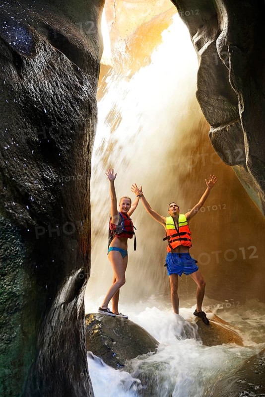 Young couple under waterfall at the canyon of Wadi Mujib