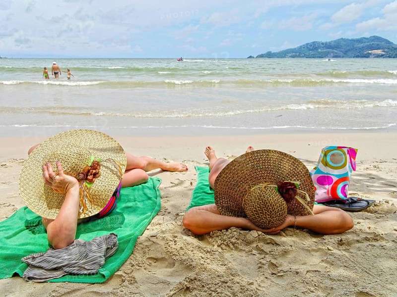 Women with large sun hats sunbathing on the beach