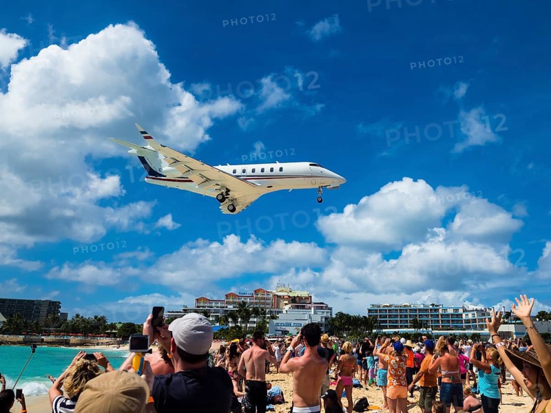 Tourists watching and photographing an airplane landing over Maho Beach