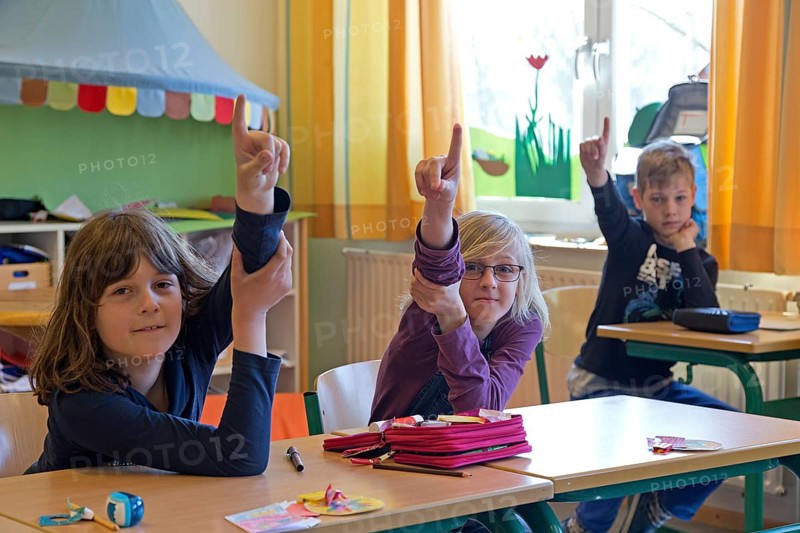 Students in elementary school with raised hands in classroom