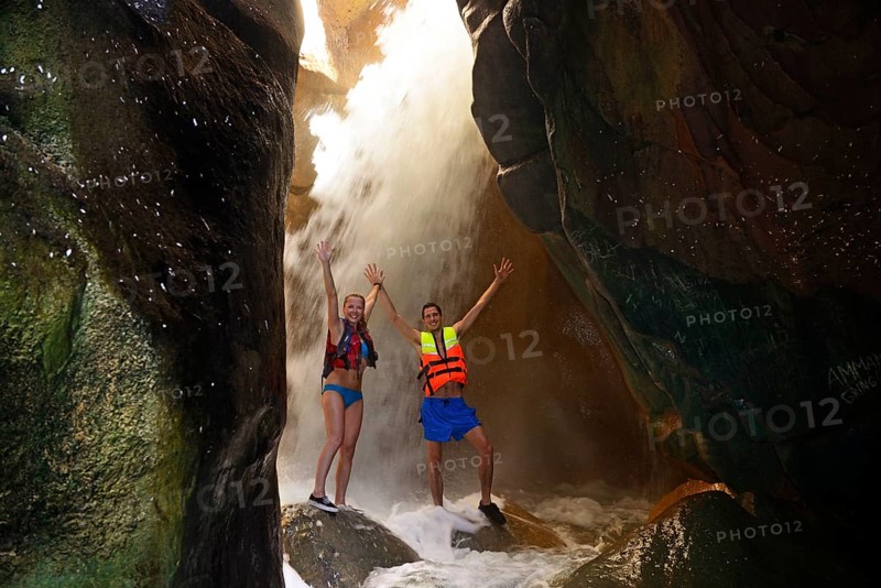 Young couple under waterfall at the canyon of Wadi Mujib