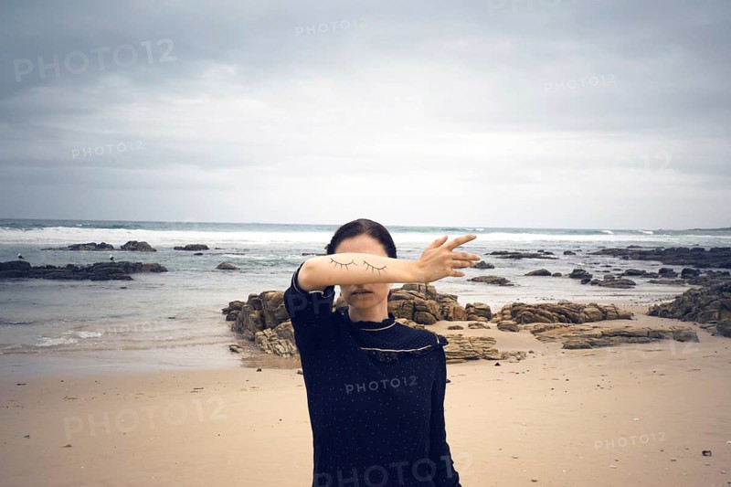Woman with closed painted on eyes on her arm standing on the beach