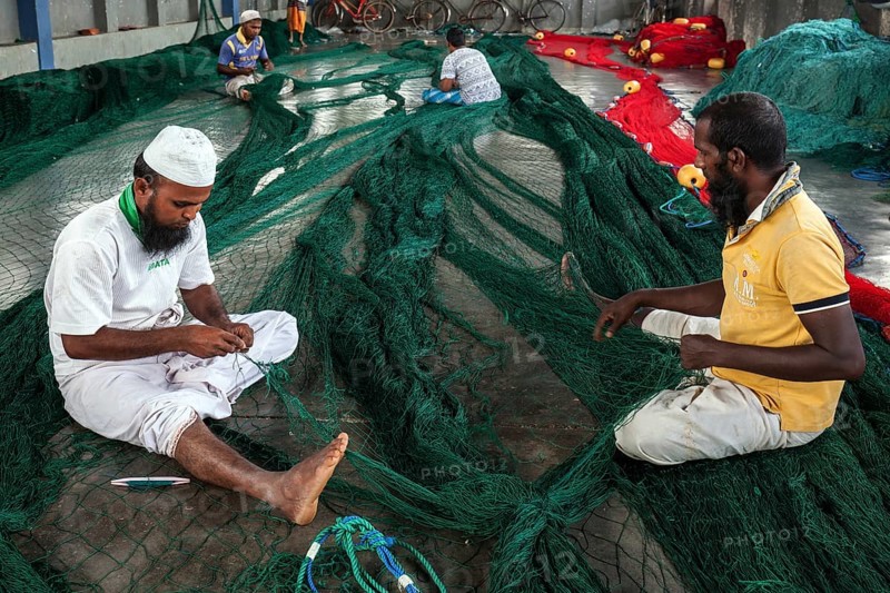 Local men repairing fishing nets in hall at harbour