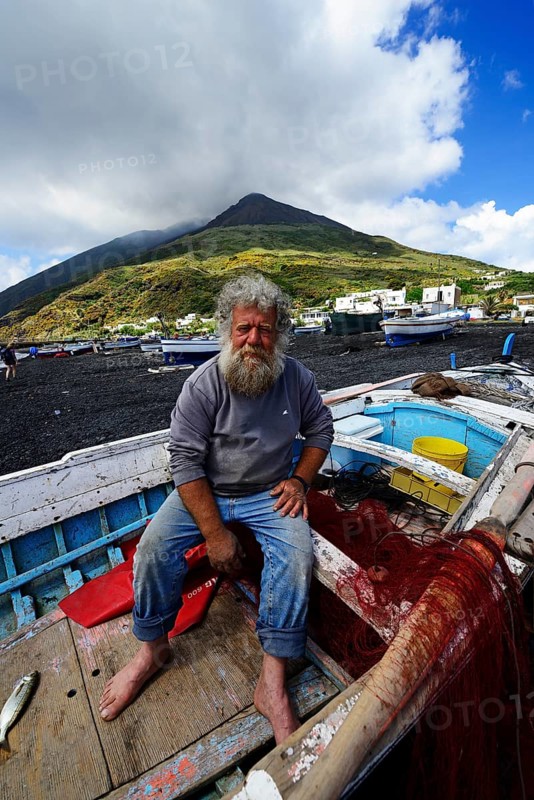 Fisherman in his boat in front of volcano on Scari beach
