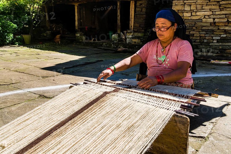 Native woman weaving blanket using sheep's wool in front of house