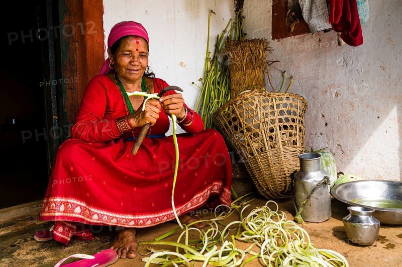 Native woman chopping vegetables in front of farmhouse