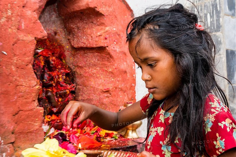 Little girl offering Prasad to statues of gods outside Khadga Devi Temple