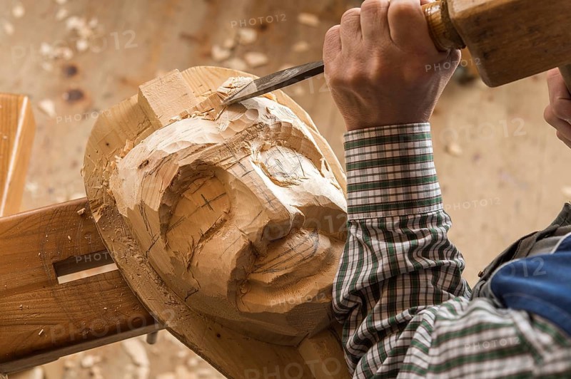 Carving the face of a wooden mask into wooden block using wood carving tools