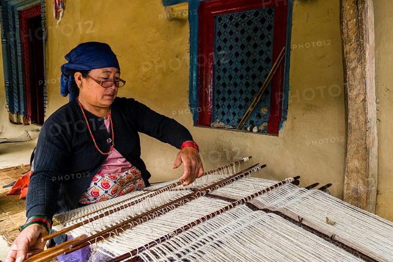Native woman weaving blanket using sheep's wool in front of house