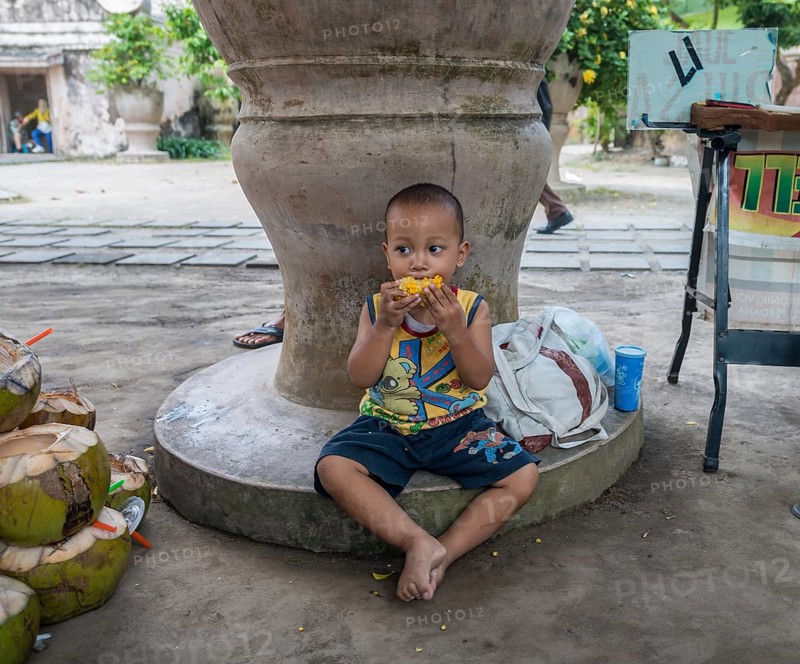 Little Indonesian boy eating grilled corn on the road side