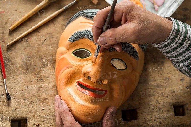 Painting the face of a wooden mask with a paintbrush