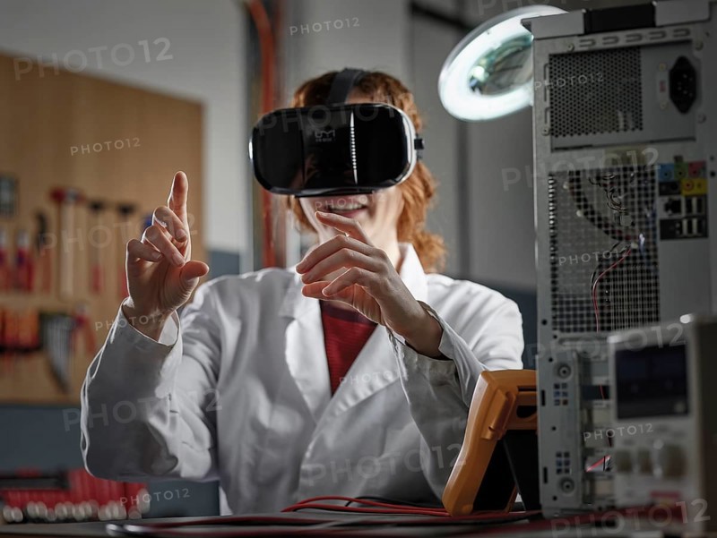 Woman with VR goggles and lab coat sitting in an electronics laboratory